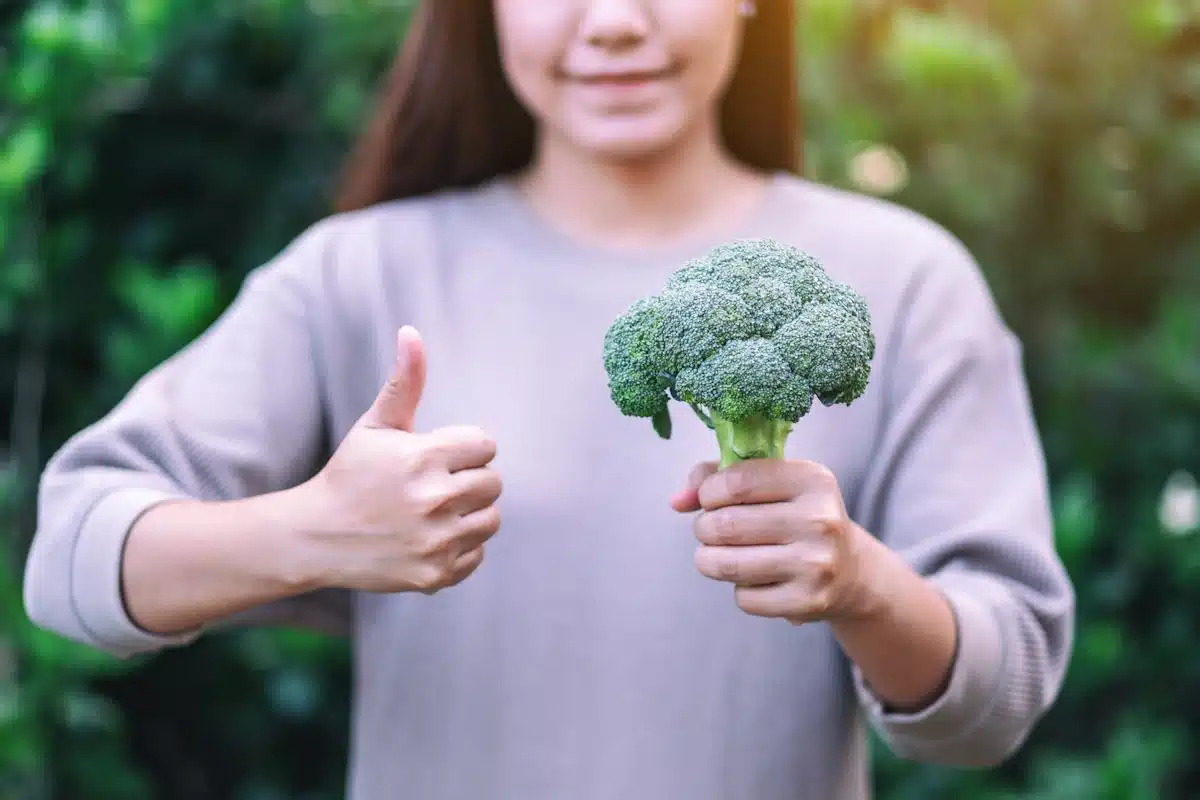 A woman holding broccoli and making thumbs up gesture