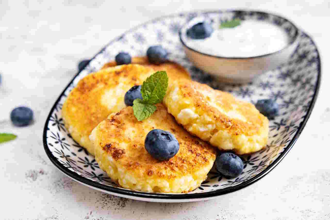 Cottage cheese pancakes with sour cream and blueberries on a light background. Breakfast or lunch