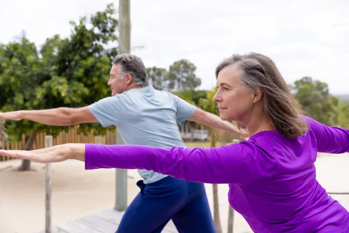 A man and a woman with arms outstretched practicing warrior 2 yoga pose at beach