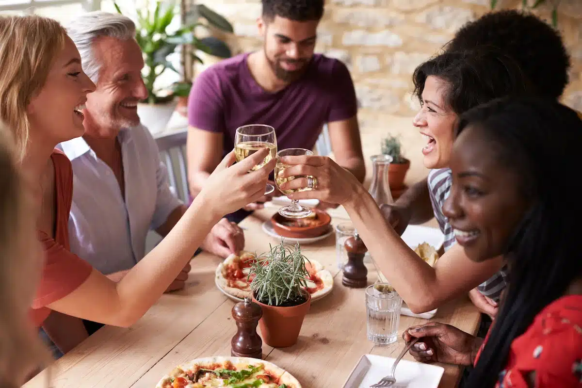 Friends laughing at a dining table while enjoying lunch in a cafe making a toast