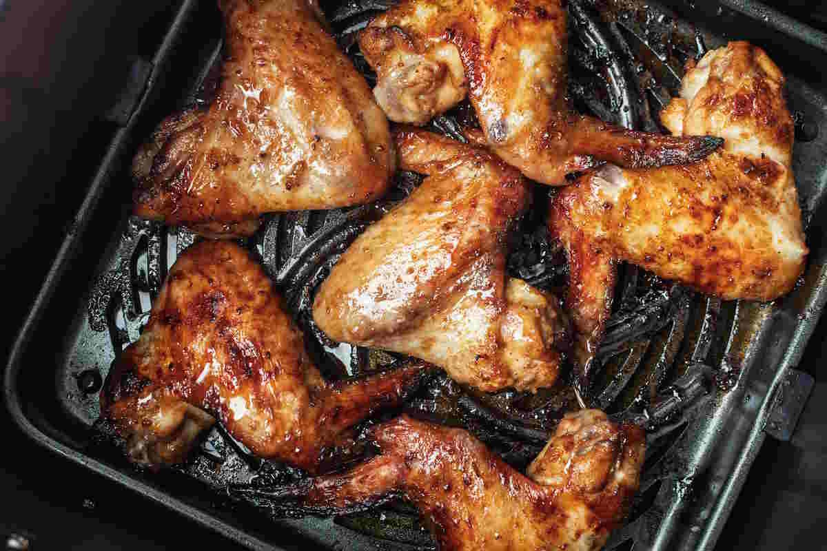 How to Reheat Chicken Wings. Close-up of caramelized chicken wings in air fryer tray, oily glaze and browned edges highlight fast dinner and snack prep.
