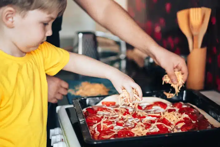 Uncle and nephew sprinkle grated cheese on pizza.