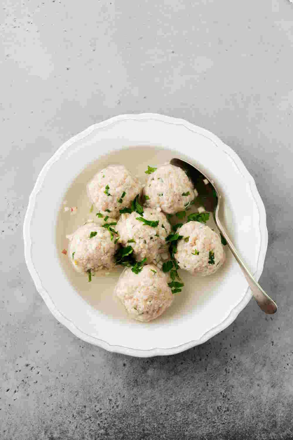 Homemade chicken matzo ball soup with parsley and garlic in simple white ceramic plate on a gray stone or concrete background. Traditional Jewish passover dish.