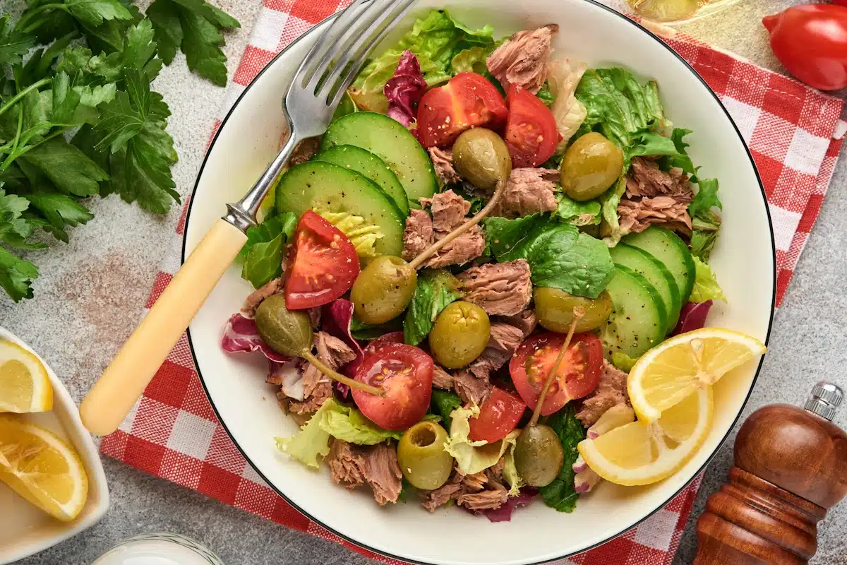 Tuna salad with fresh vegetables, olives, capers and lemon served in bowl on light grey background