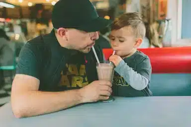 Photo of a father and son sharing a milkshake at a retro diner at lunch