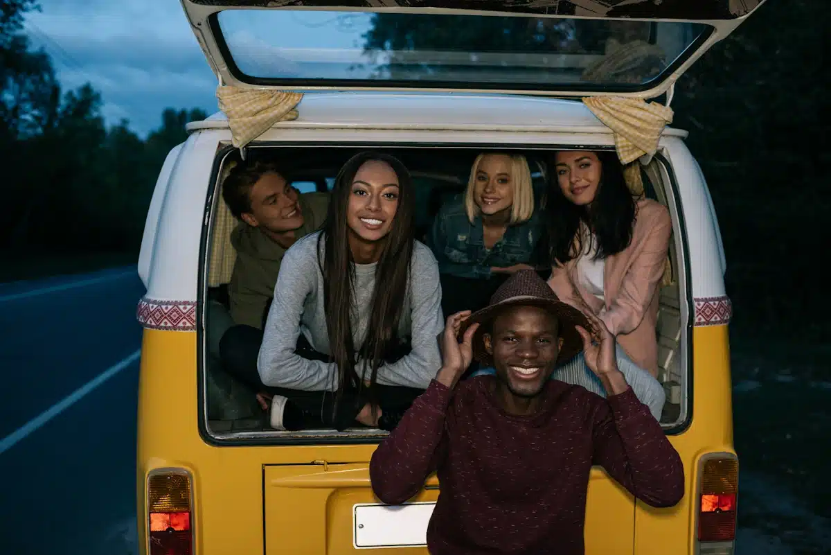 multiethnic friends traveling together on retro minivan on a road trip