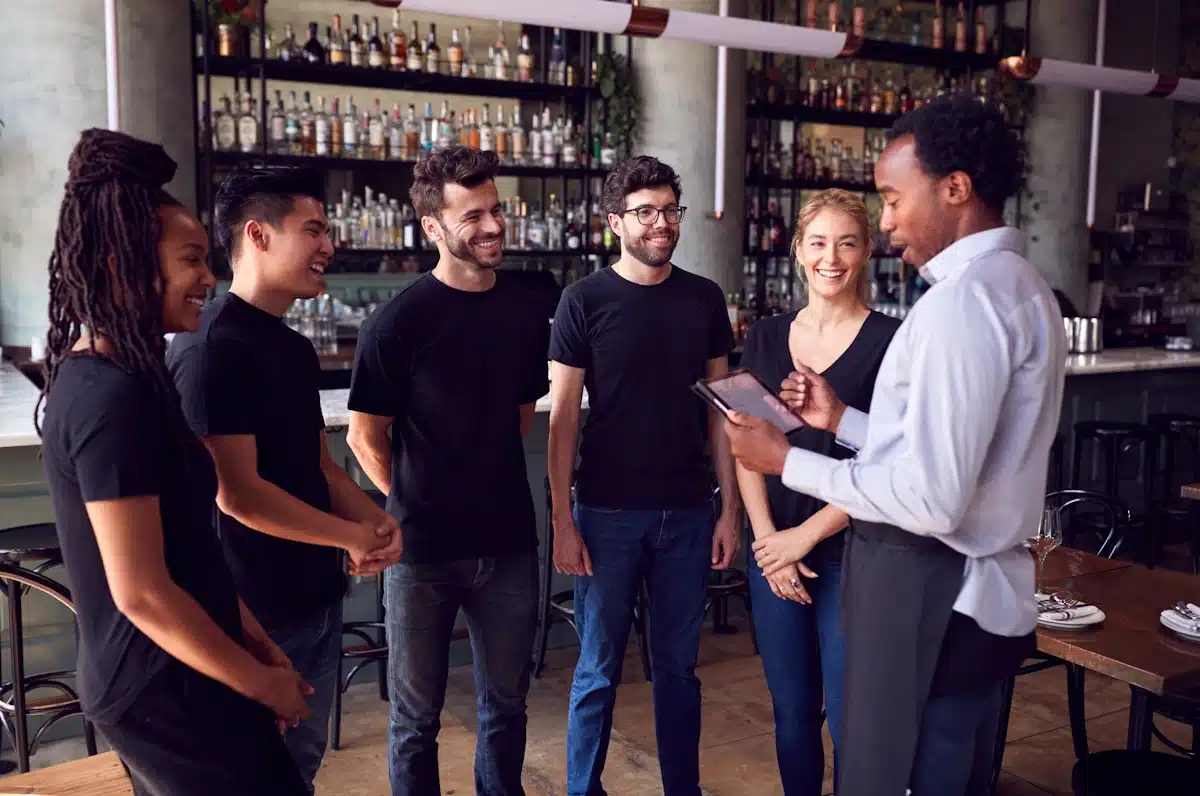 Male Local restaurant owner With Digital Tablet Giving Team Talk To Wait Staff of three men and two women