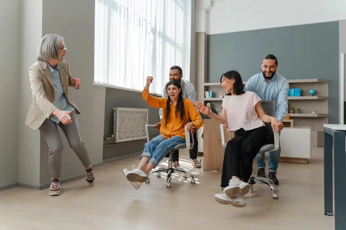 Reinvigorating office lunch culture with Two women on chairs being pushed by two men across the finish line in an office Olympic event