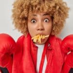 A woman wearing boxing gloves with a mouthful of french fries symbolozes how power lunches are transforming your workday