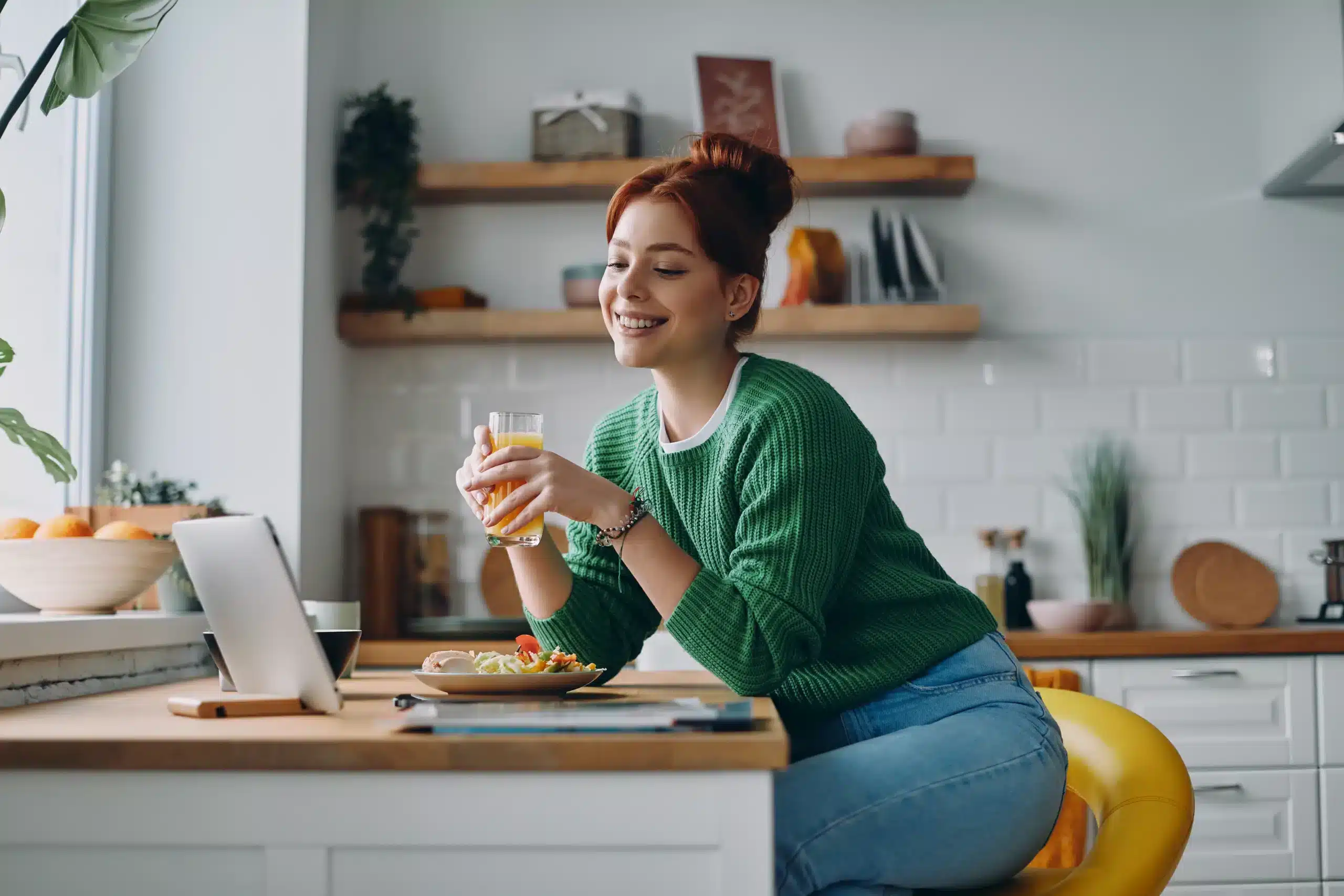 Woman sitting at her kitchen counter having lunch while in a meeting looking for lunch ideas for teleworkers