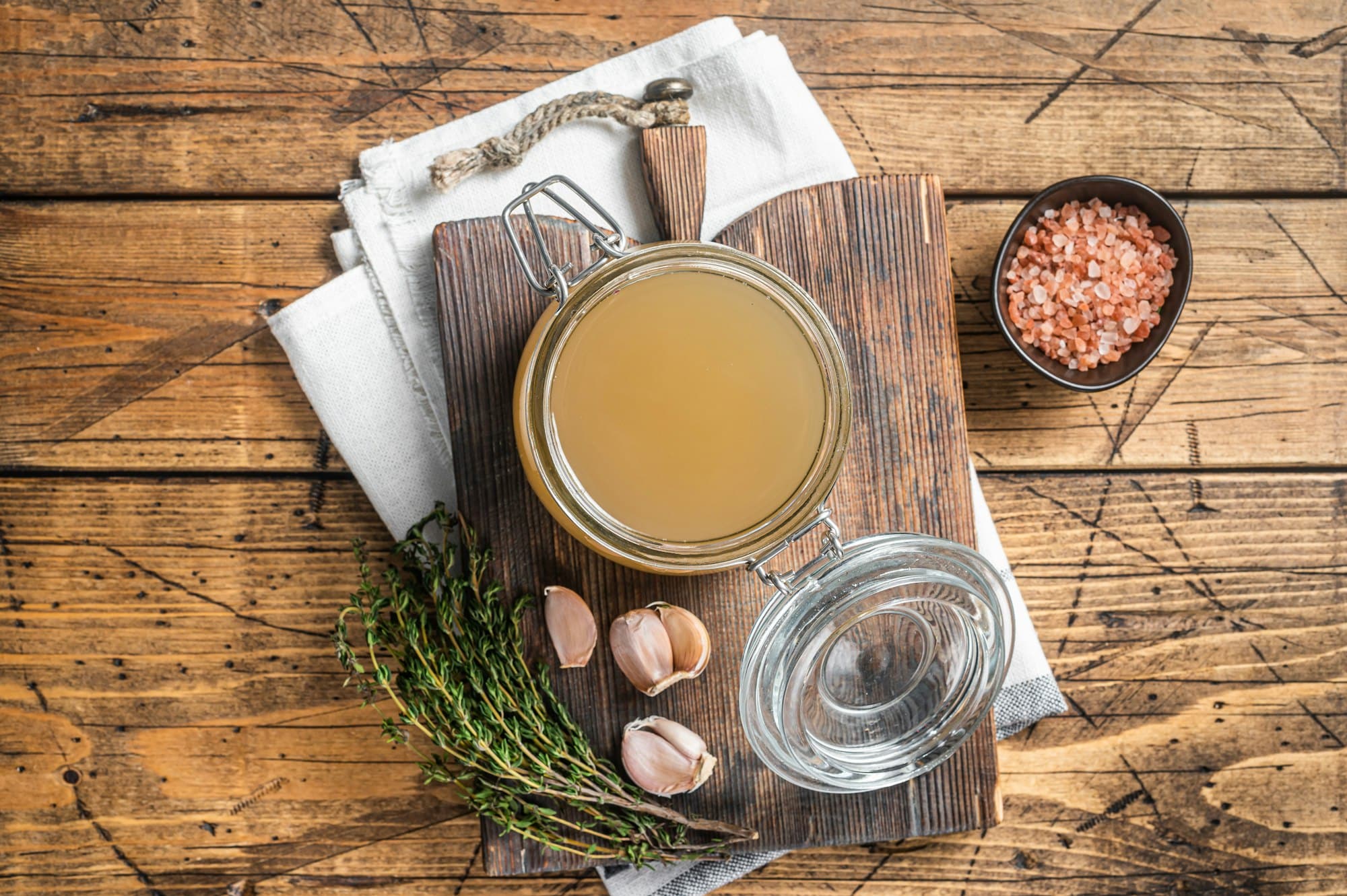 Bone broth for chicken soup in a glass jar. Wooden background. Top view