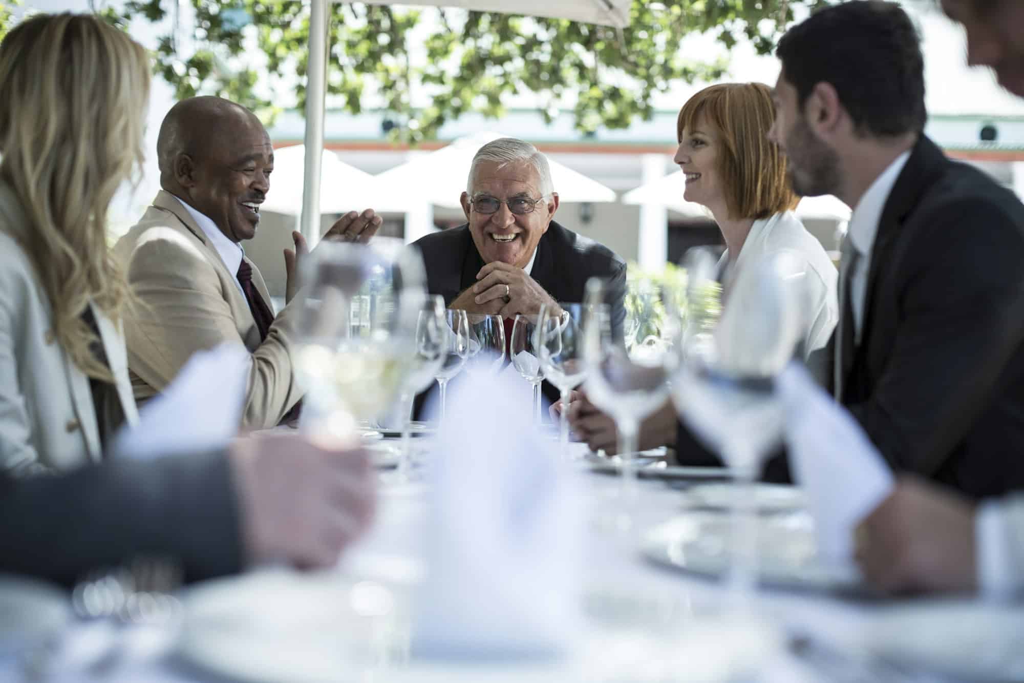 Business people having business lunch in restaurant, three men and two women seated at the table laughing together