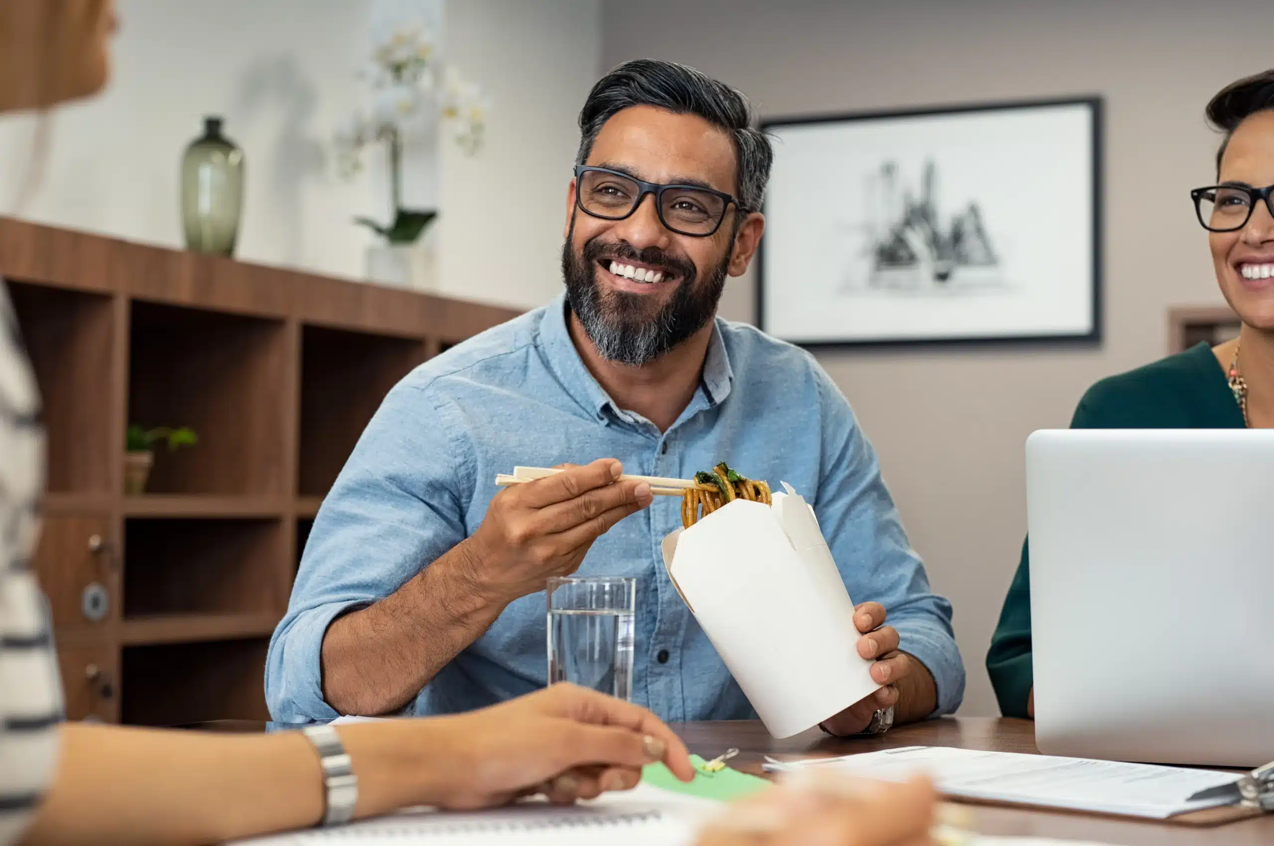 A man eating a noodle lunch at work from a takeout box using chopsticks