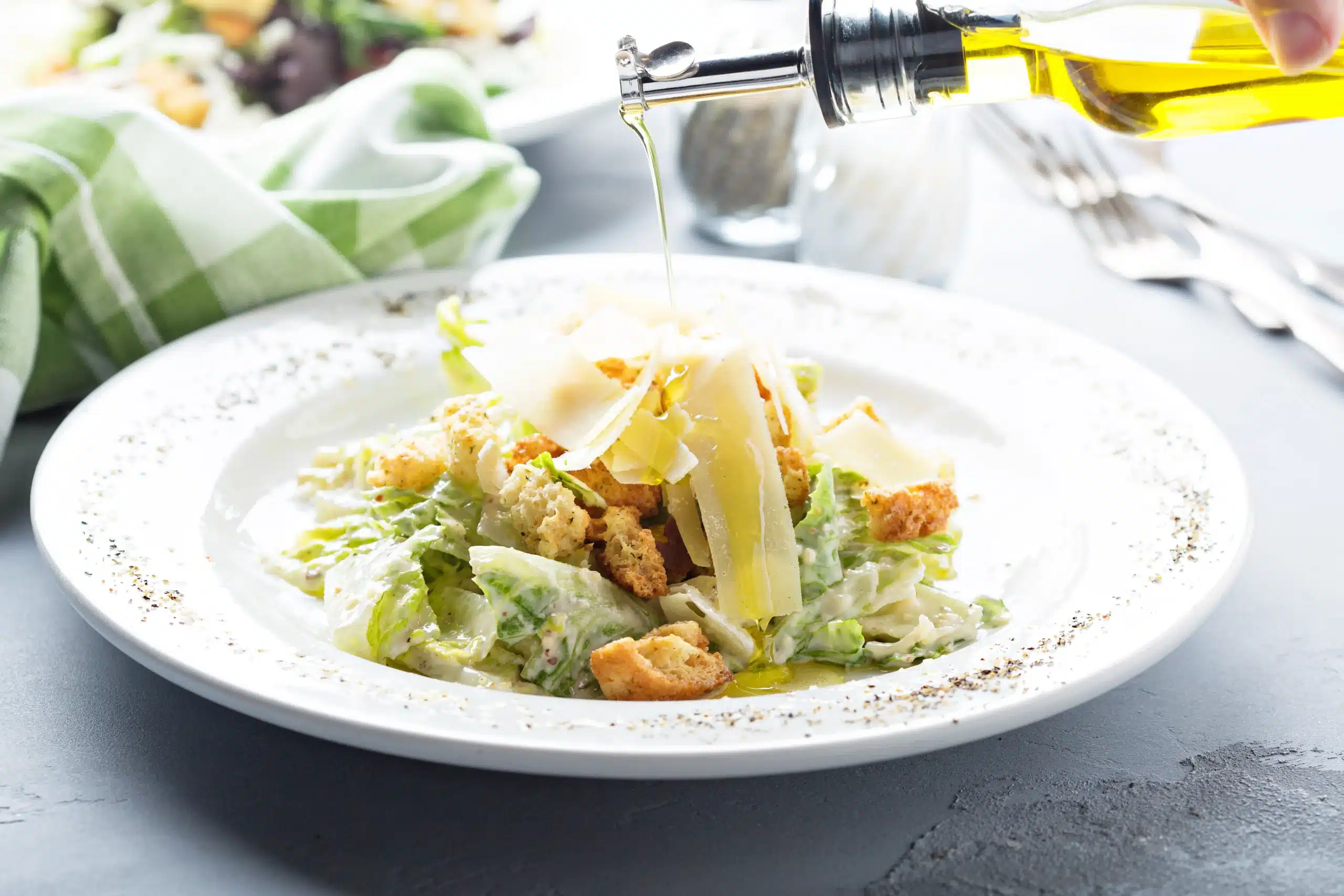 A lovely classic Caesar Salad in a bowl as someone pours oil into it