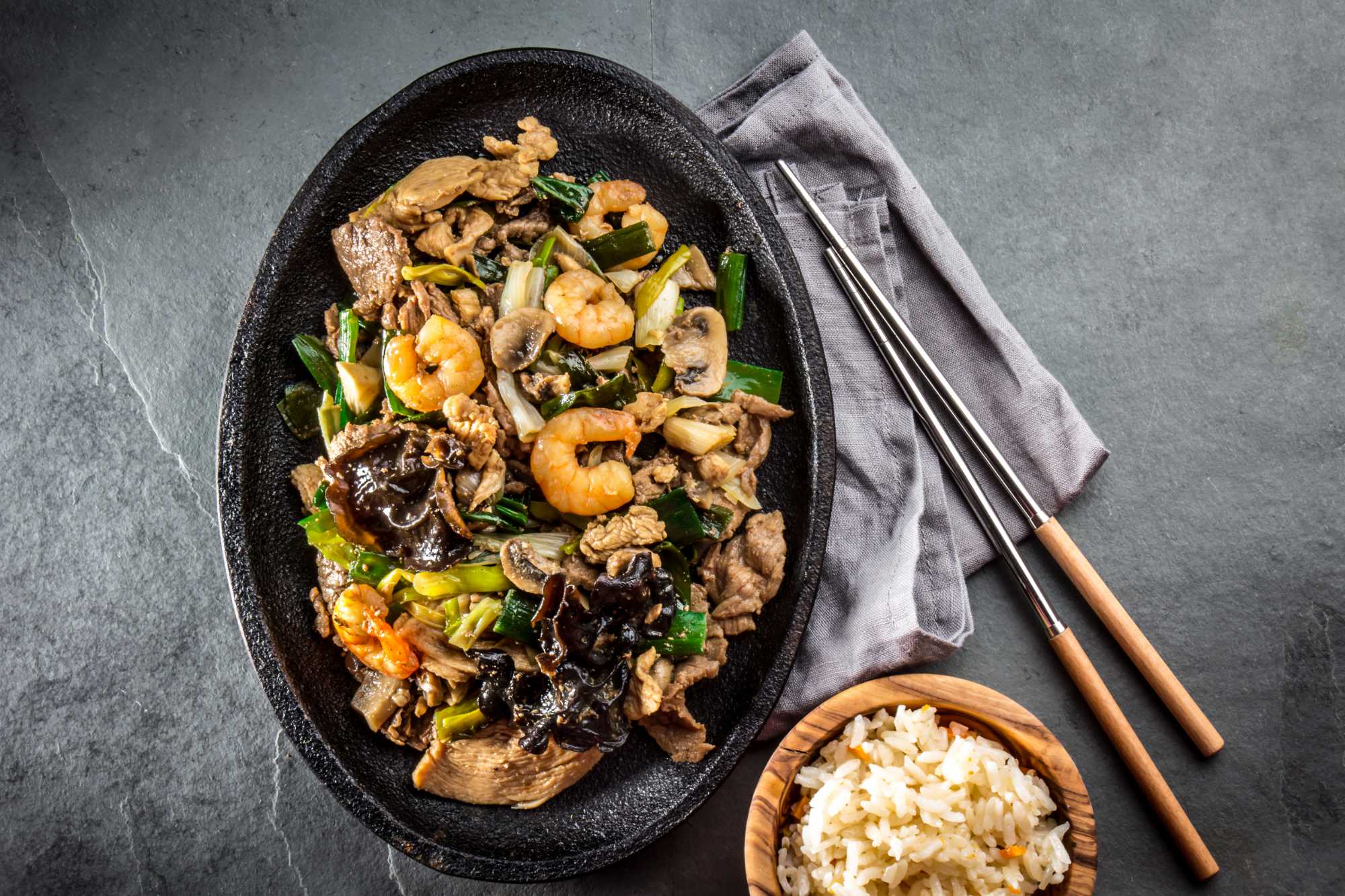 Pan of fried beef, pork, chicken, shrimp, shiitake mushrooms and spring onion. Parillada china served with rice on gray slate background.