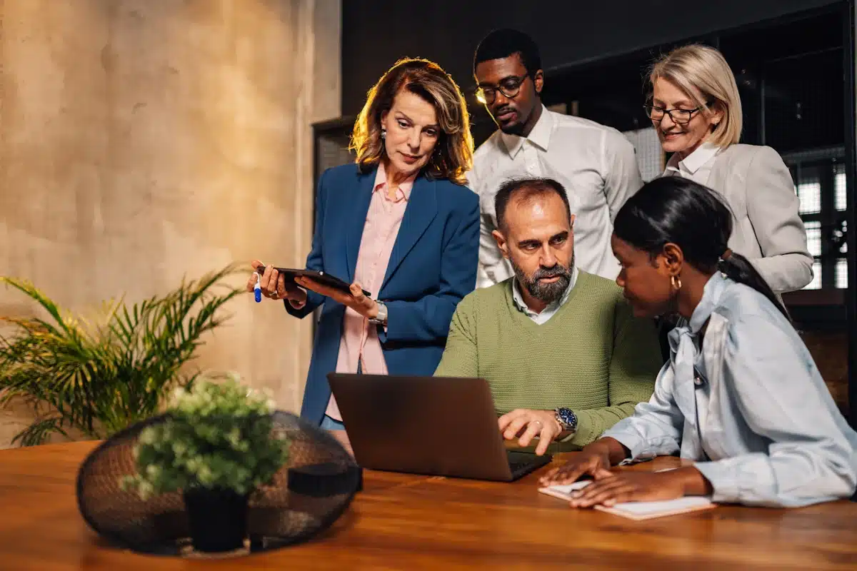 Three women and two men collaborating on a team challenge huddled around a laptop computer.