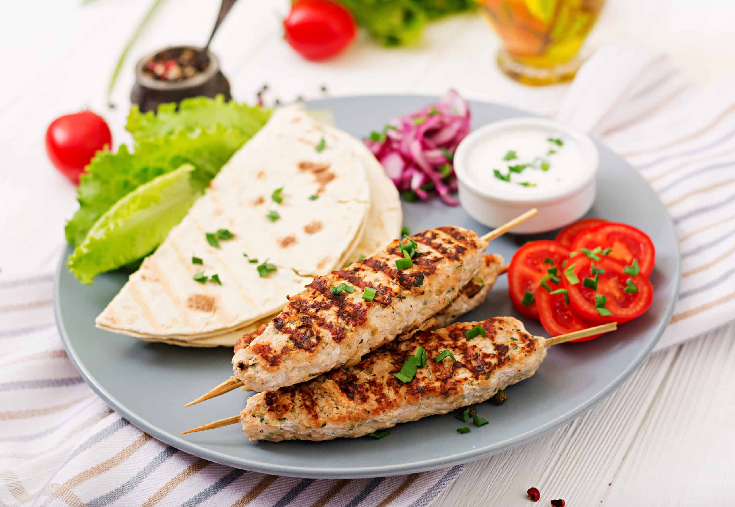 Grilled chicken skewer with pita and fresh vegetables.