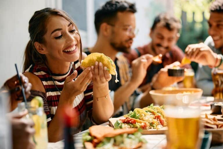 The Health Benefits of Having Lunch With Friends with a Happy woman eating tacos during a lunch with friends in Mexican restaurant.