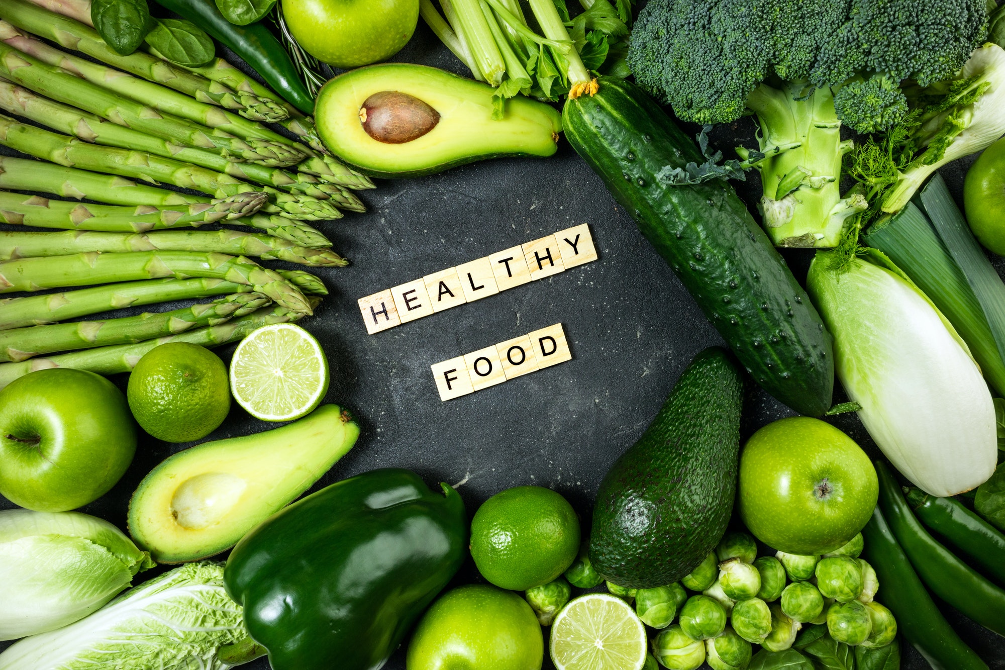 Various green fruits and vegetables surrounding the words healthy food