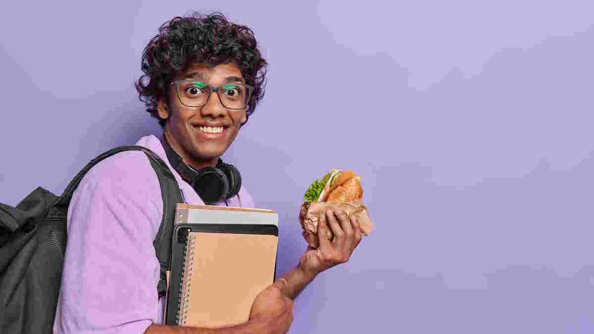 healthy lunch for teens Teen holding sandwich and notebooks.