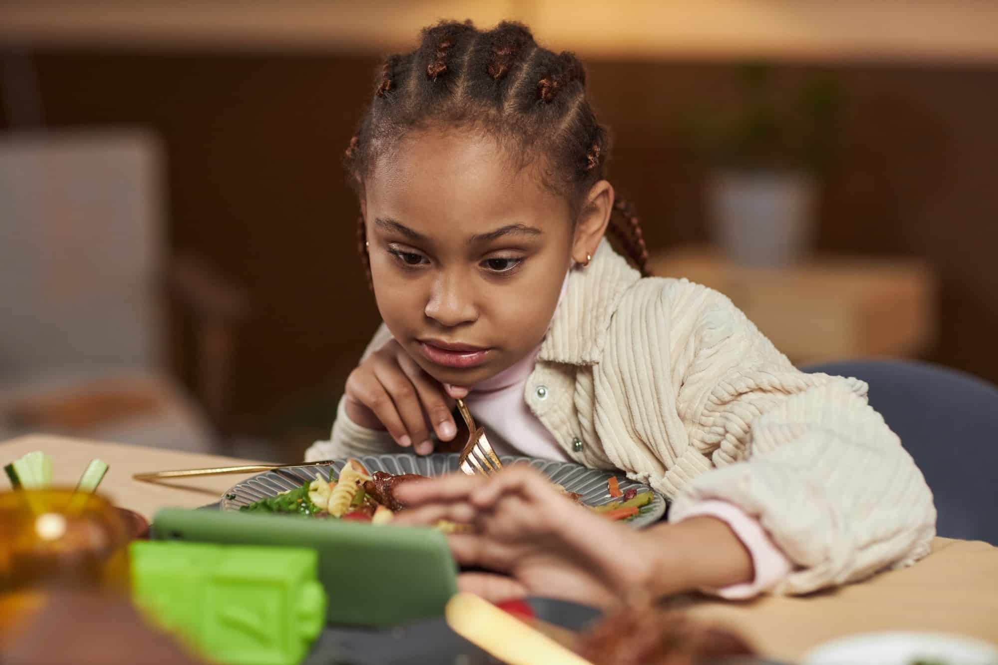 Little Girl Using Smartphone While Eating at Dinner Table