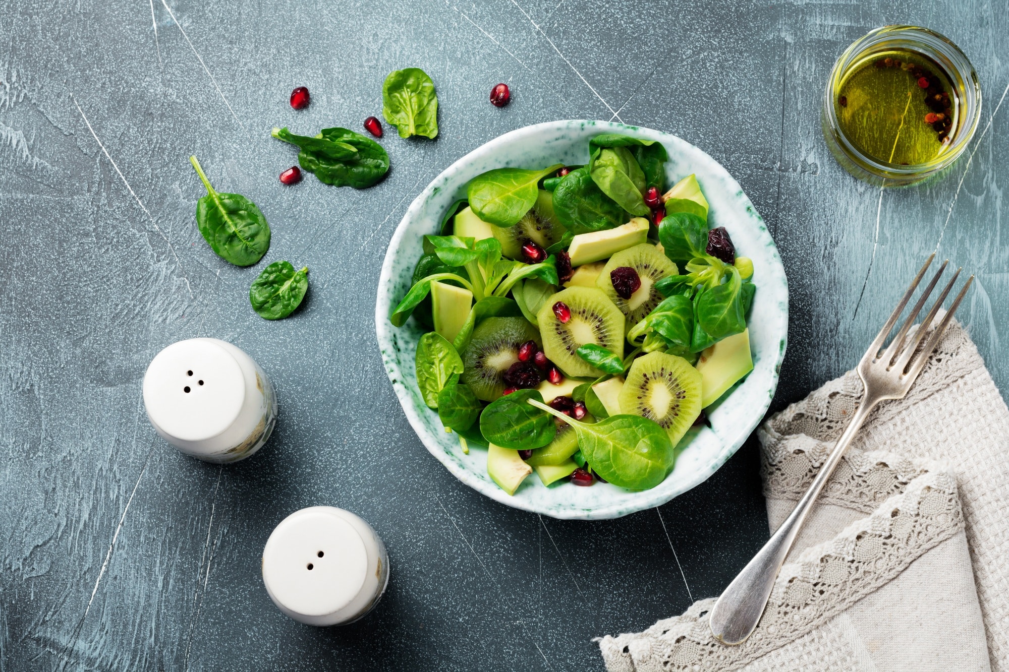 Salad of spinach baby leaves, watercress, kiwi, avocado and pomegranate in an old ceramic plate on a