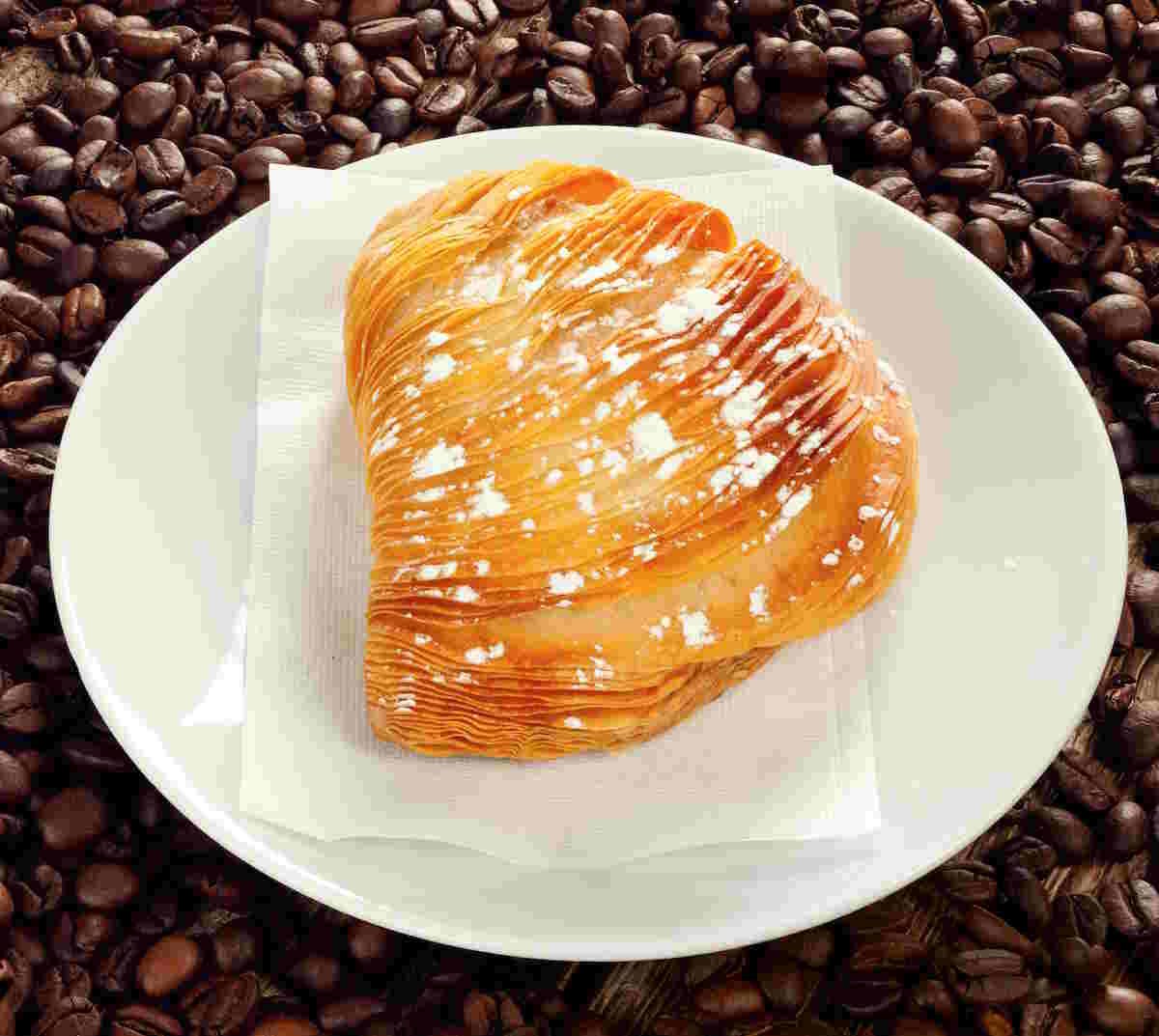 Delicious, traditional Sfogliatelle Lobster Tails | Low-Carb & Diabetic-Friendly pastry dusted with powdered sugar, served on white plate over coffee beans background