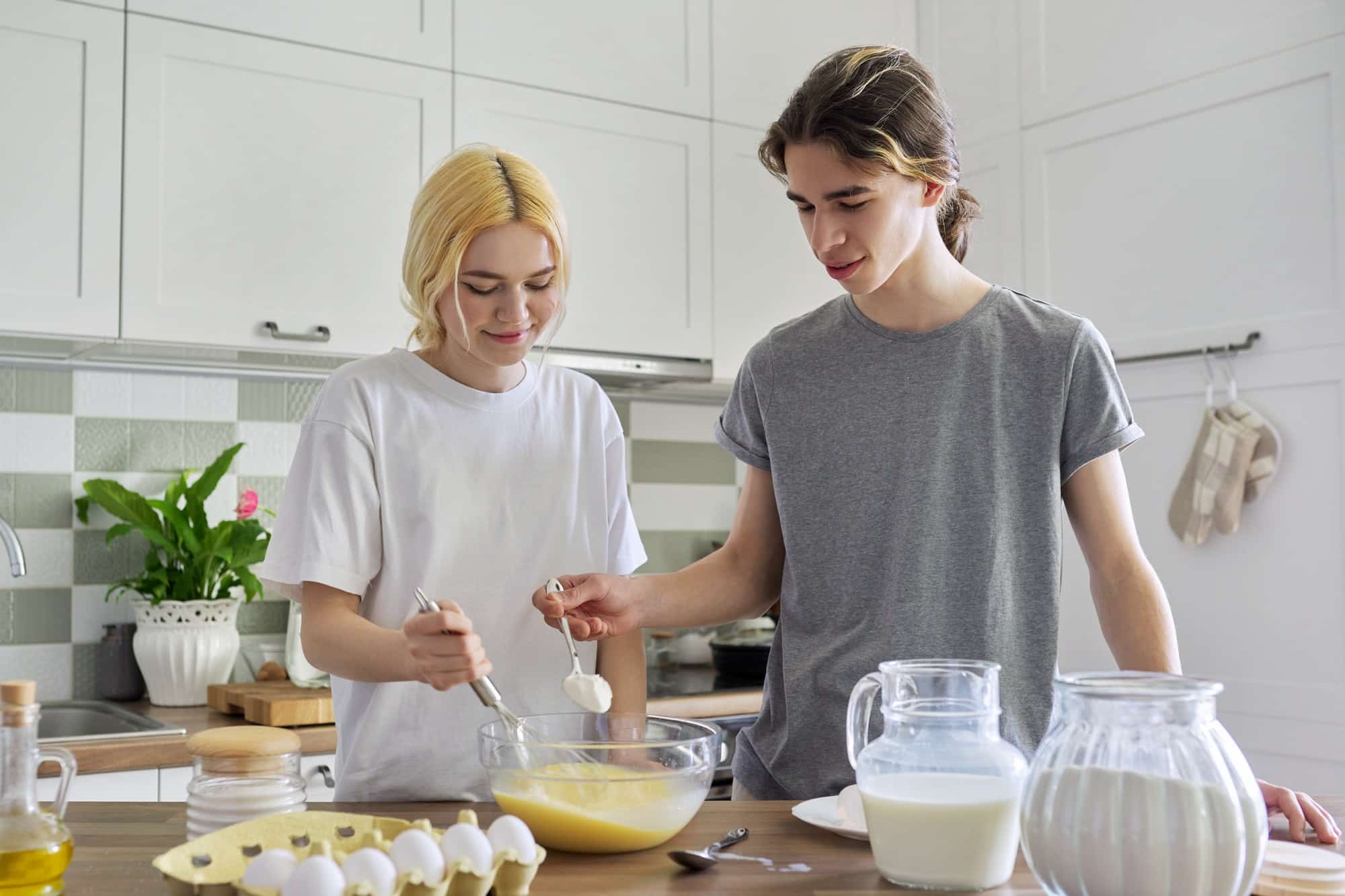 Teenagers: a guy and girl cooking pancakes in kitchen together